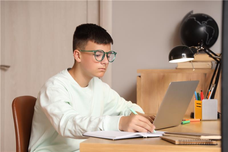 Teenager studying online with laptop and notebook at desk