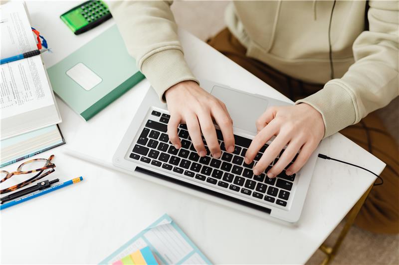 Young student studying online with notebook and laptop at home.